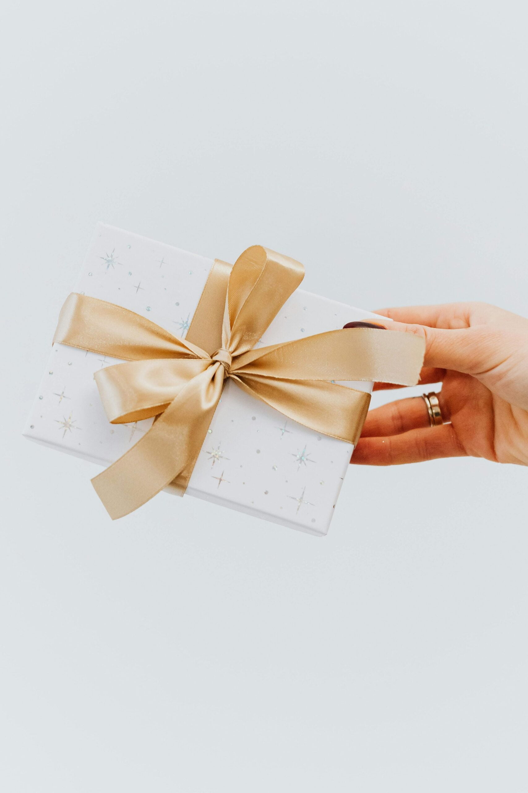 main qui tient un joli cadeau blanc avec un beau ruban doré, présent emballé avec soin